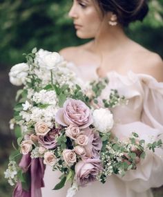 a woman holding a bouquet of flowers and greenery in her hands while wearing an off the shoulder dress