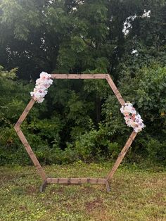 a wooden hexagonal frame with flowers on it in front of some trees and bushes