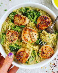 someone holding a fork in a bowl of pasta with scallops and broccoli