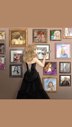 a woman in a black dress is looking at pictures on the wall and holding a tablet