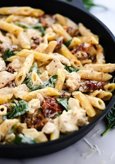 a skillet filled with pasta and spinach on top of a white countertop