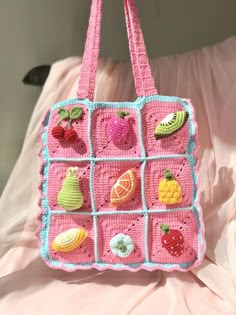 a pink crocheted purse with fruits and vegetables on the front, hanging from a hook