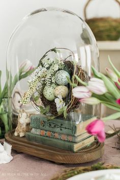 an arrangement of flowers and books under a glass dome