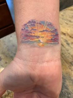 a person's hand with a small tattoo on the wrist that has an image of a sunset