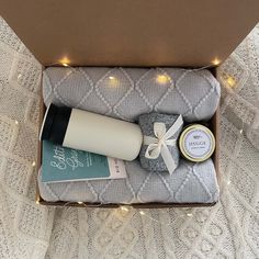 an open box with items inside on a white blanket and string lights around the package