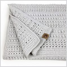 a white crocheted blanket with a brown button on the end and two pillows sitting next to it