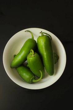 three green peppers in a white bowl on a black table