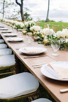 a long table set with white plates and place settings for an outdoor wedding reception in the grass