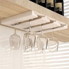 four wine glasses hanging from a shelf in a kitchen with white cabinets and wooden shelves