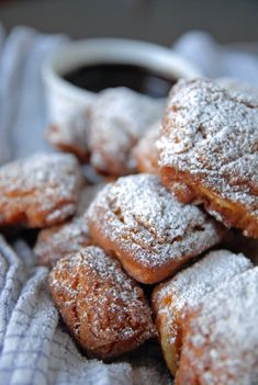 powdered sugar covered pastries are piled on top of each other with a cup of coffee in the background