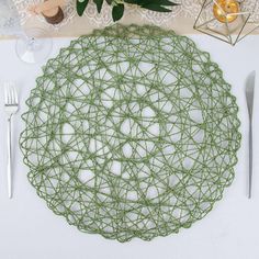 a place setting with green yarn and silverware on a white table cloth, surrounded by greenery