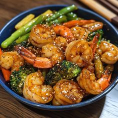 a blue bowl filled with shrimp, broccoli and carrots