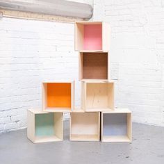 four cubes are stacked up against a white brick wall in an empty room with concrete flooring