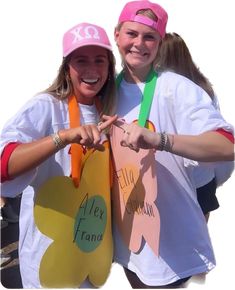 two women in matching shirts and hats posing for the camera with carrots on their hands