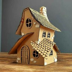 a cardboard house made to look like it is on top of a wooden table with a gray wall in the background