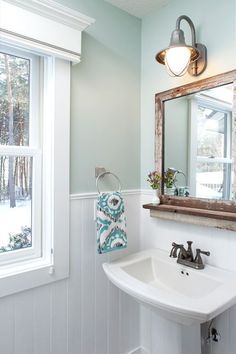 a white sink sitting under a mirror in a bathroom next to a window with shutters