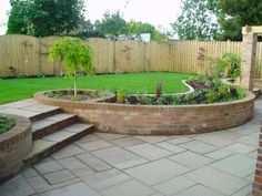 a garden with steps leading up to the grass area and trees in the back yard