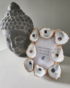 there is a small buddha statue next to a vase with shells on it and a plaque that says, the world is your oyster oyster