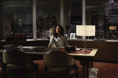 a woman sitting at a desk in front of a window with the city lights behind her