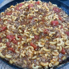 a skillet filled with macaroni and cheese on top of a wooden table