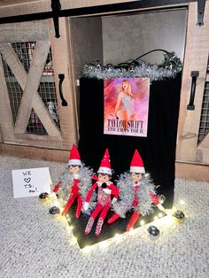 three elfs are sitting on the floor in front of a sign and some christmas lights