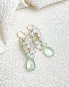 These are a luxe little adornment for your ears! Enjoy the indulgent shimmer of petite prehnite, moonstone, and crystal quartz clusters all crowning ethereal faceted prehnite briolettes. Each hand-picked gem is accented and hand-wrapped in 14k gold-fill. The gold-filled ear wires are smooth and comfortable for effortless wear. What I love the most about these earrings is the soft green and white colors. These can be worn festively for the holidays, but also will carry you through your spring and summer styles. Earrings drop about 1.5 inches Materials: prehnite briolettes and beads rainbow moonstone beads crystal quartz beads 14k gold-filled ear wires and components Elegant Prehnite Gemstone Jewelry, Moonstone Crystal, Moonstone Beads, Quartz Beads, Summer Styles, Quartz Cluster, White Colors, Earrings Drop, Cluster Earrings