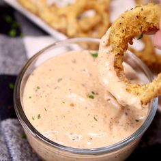 a person dipping onion rings into a small glass bowl filled with ranch dressing and garnished with parsley