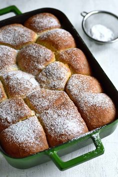 a green pan filled with bread covered in powdered sugar on top of a white table