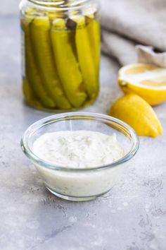 pickles and yogurt in a glass bowl next to jars with lemons