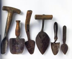 five different types of tools hanging on a white wall, one is old and the other has wood handles