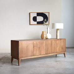 a wooden sideboard with two vases and a painting on the wall behind it