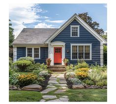 a blue house with red door surrounded by flowers and greenery in the front yard