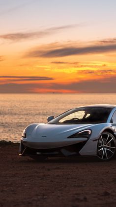 a white sports car parked in front of the ocean at sunset or sunrise with clouds