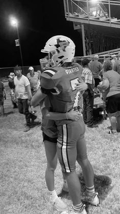 two football players embracing each other on the field at night time with fans in the background