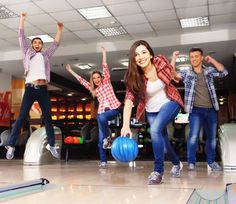 group of young people playing bowling in an indoor bowling alley with their arms up and one holding a blue ball