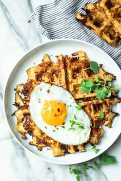 a plate with waffles and an egg on it next to a hand holding a fork