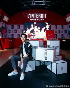 a man sitting on top of a pile of boxes in front of a red wall