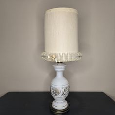 a white table lamp sitting on top of a black table next to a gray wall