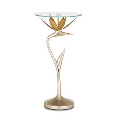 a table with a glass top and gold metal flower design on the base, against a white background