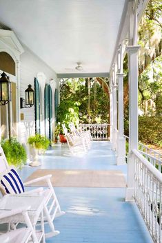 a porch with white rocking chairs and potted plants