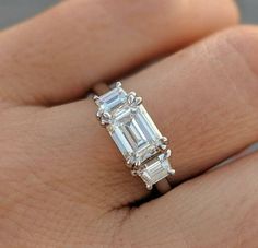 a woman's hand with a diamond ring on top of her finger and an emerald stone in the middle