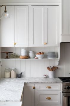 a kitchen with white cabinets and marble counter tops, gold pulls on the cupboards