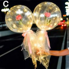 two clear balloons with roses on them being held by someone's hand at night