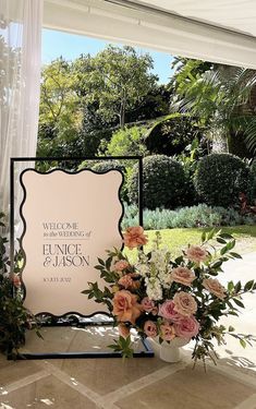 a welcome sign with flowers and greenery in front of the entrance to a garden