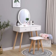 a white dressing table with a mirror and stool in front of a potted plant