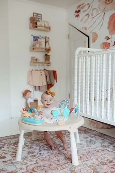 a baby sitting in a high chair with toys on it's feet and looking at the camera