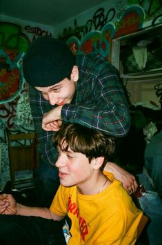 two young men sitting next to each other in front of a wall covered with graffiti