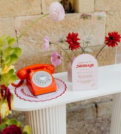 an orange phone sitting on top of a white table next to red and pink flowers