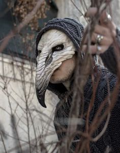 a man with a bird mask on his face is standing in front of some branches