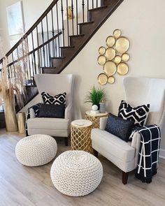 a living room with white chairs and black and gold pillows on the floor next to a stair case